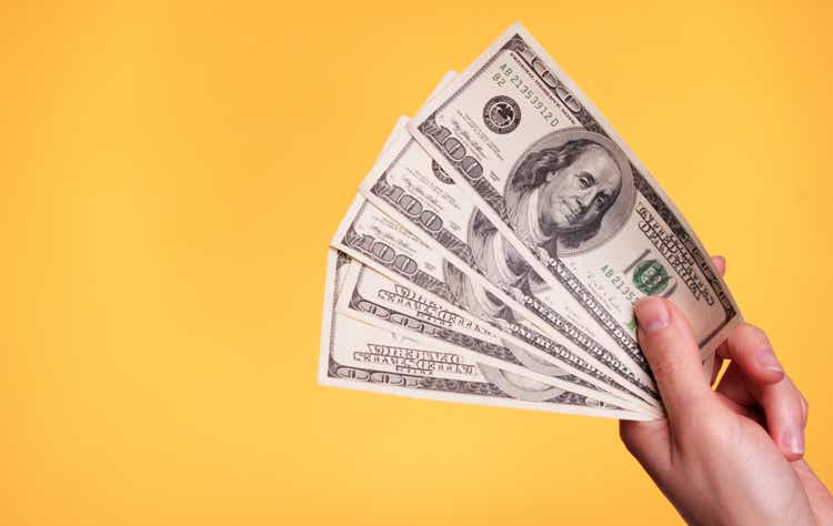 A hand holding five $ 100 bills