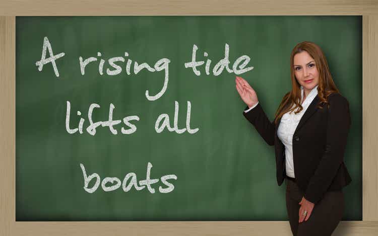 Teacher showing A rising tide lifts all boats on blackboard