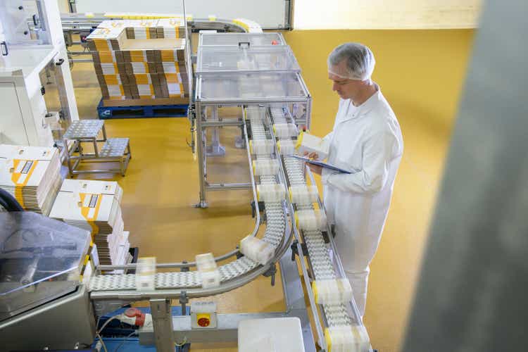 Worker inspecting packed products on conveyor belt in biscuit factory