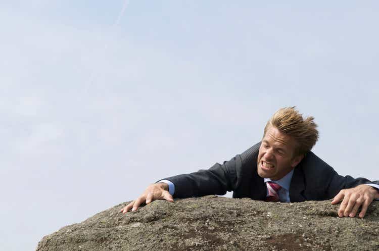Struggling Businessman Clinging to Edge of Windblown Rock