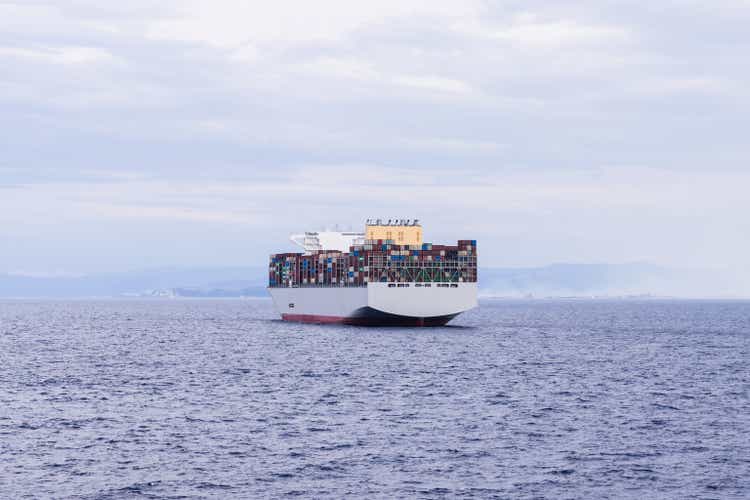 Photo of a large cargo ship in the middle of the sea loaded to the top with containers of all colors.
