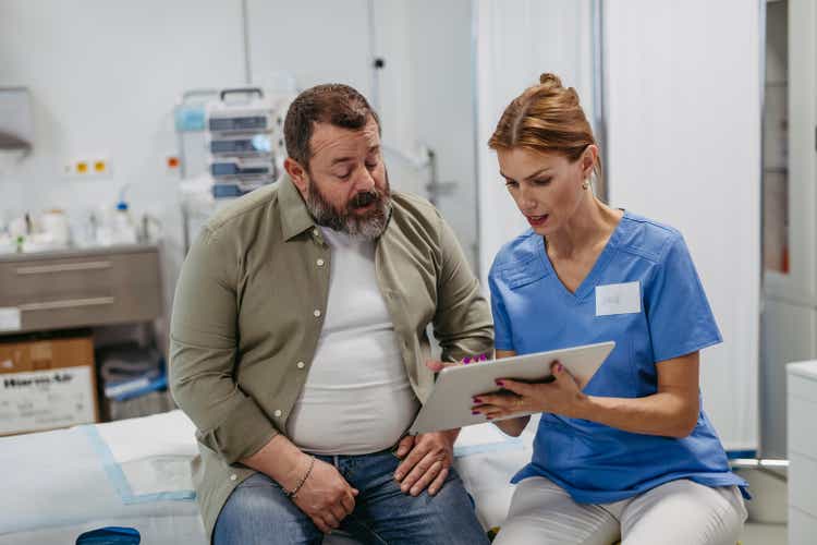 Female doctor consulting with overweight patient, discussing test result in doctor office. Obesity affecting middle-aged men"s health. Concept of health risks of overwight and obesity.
