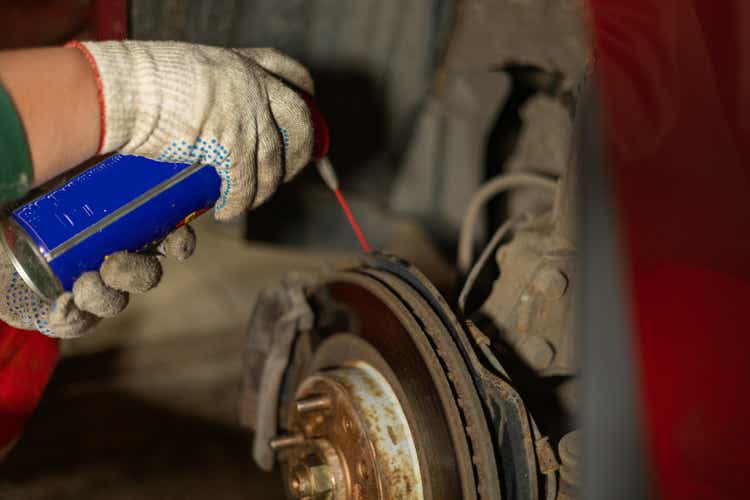A man is repairing a car in a garage. A man treats rusted bolts with WD-40 solution. Replacing a brake disc on a car in the garage. Concept of a man fixing his car in a garage.