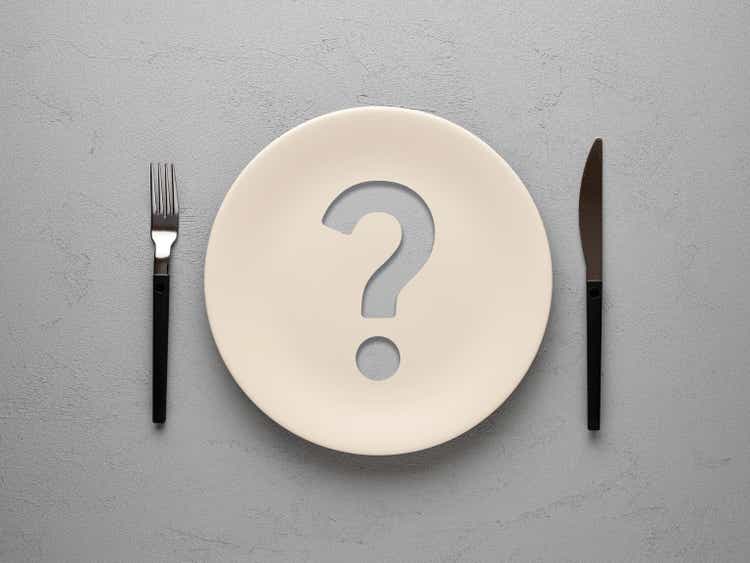 Ceramic plate with question mark on textured gray background. Diet and nutrition concept.