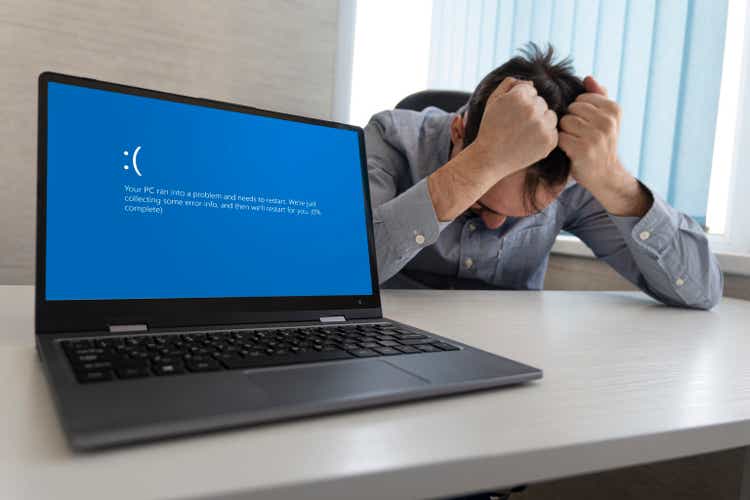 showing error blue screen on Laptop against the background of an angry upset man clutching his head