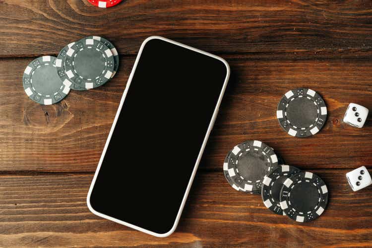 Poker chips and smartphone on wooden table