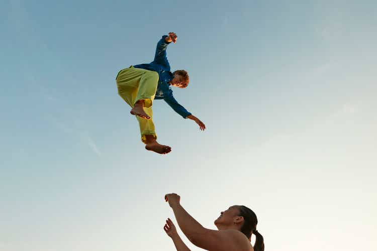 Woman looking at friend jumping high up in sky