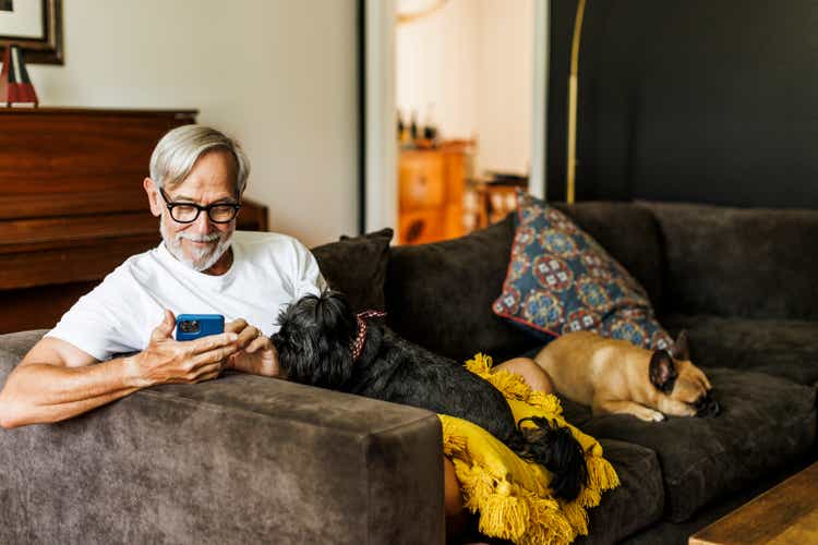 Smiling senior man using mobile phone while sitting with dogs on sofa at home