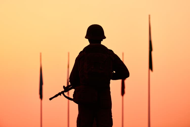 Rear view of silhouette of soldier in military gear holds weapon against bloody sunset