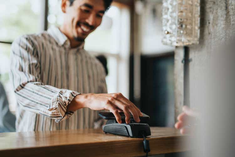 Smiling businessman making contactless payment at checkout counter in restaurant