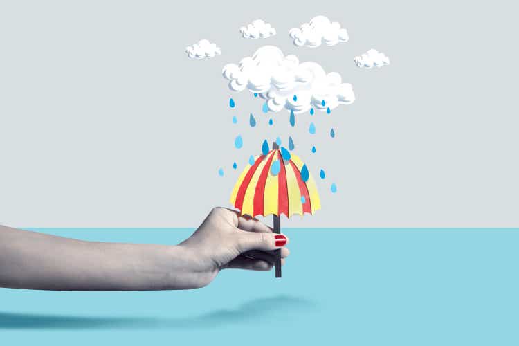 Hand holding paper umbrella under rain cloud