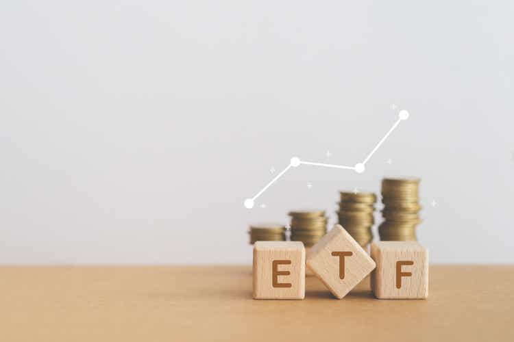 Abrevierea ETF pentru Exchange Traded Fund scrisă pe blocuri de cuburi de lemn cu teanc neclar de monede și linie grafică în creștere albă. Spațiu de copiere inclus