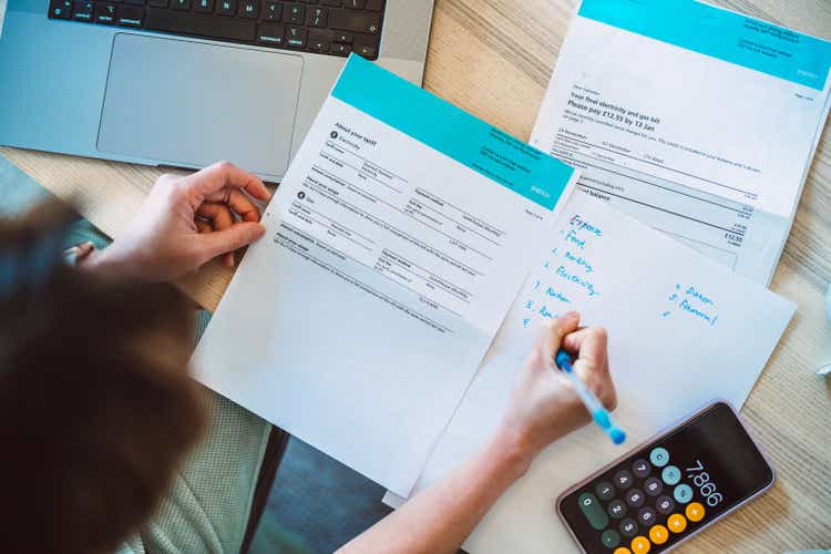 Top view of young Asian women managing household finances using laptop and smartphone. She works on utility bill and calculates household expenses.