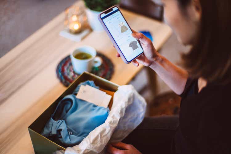 Young woman doing online shopping for clothes on smartphone at home