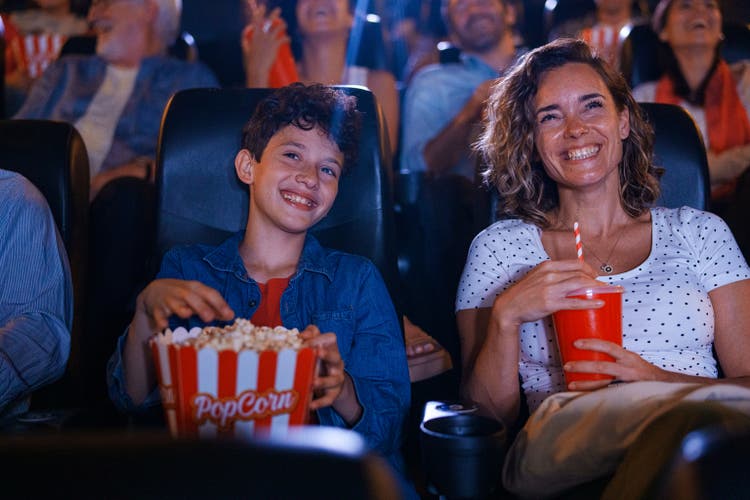 Mid-shot of cheerful young boy and his mother having fun at the movies