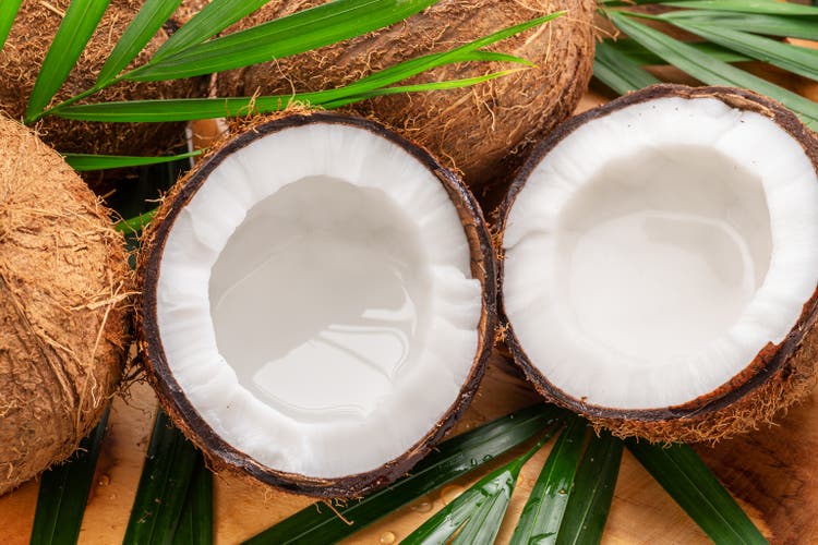 Fresh opened coconuts along with whole coconuts and coconut leaves on a wooden table. Nice fruit exotic background for your projects.