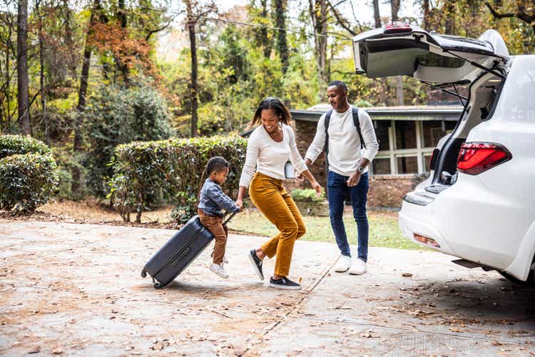 Mother pulling young boy on suitcase and loading car for family vacation