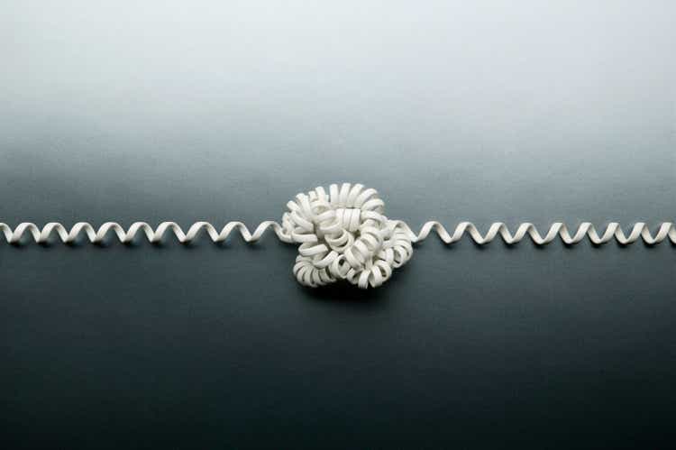 Coiled telephone cord tied in a knot on gray background