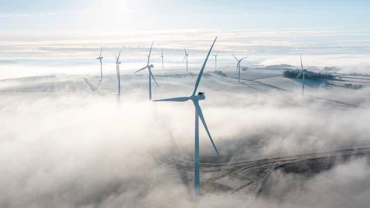 A drone/aerial view of a wind farm of wind turbines sitting proud above the low lying mist on a winter