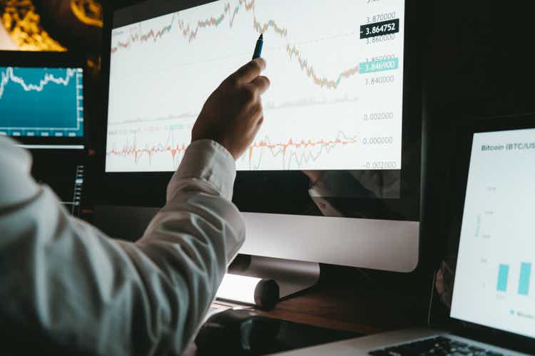 Close-up of male financial broker pointing computer monitor while analyzing stock market data in night office