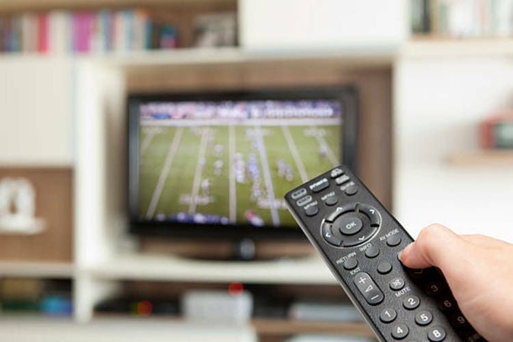 watching football with TV remote control in hand