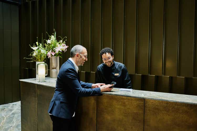 Wide shot hotel manager helping businessman at hotel front desk