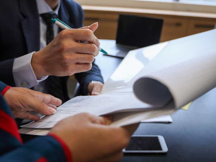 An Asian executive holds a pen and signs a document held by an Asian secretary.  Only human hands are shown, no faces.