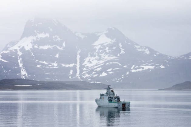 Danish Navy Patrol ship HDMS Ejnar Mikkelsen surrounded by snow capped mountains in the sea inlet leading to Nuuk, Greenland