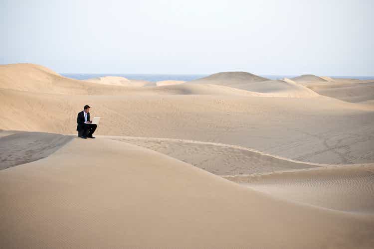 Man working on laptop sitting on a sandy desert hill