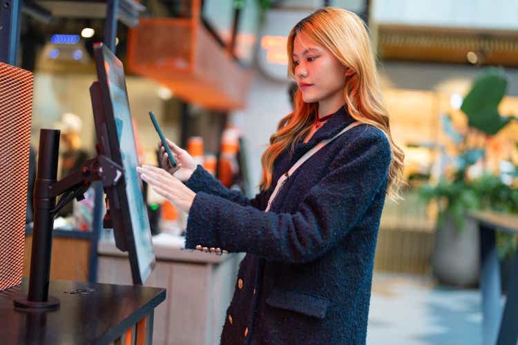 young asian female using mobile for payment on kiosk