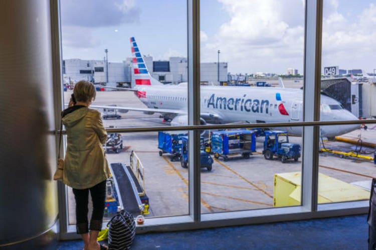 Close-up view of woman talking on mobile phone at the airport with American Airlines plane in the background.