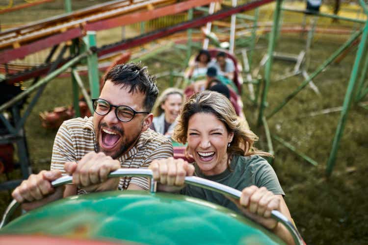 Casal alegre andando na montanha-russa em parque de diversões.