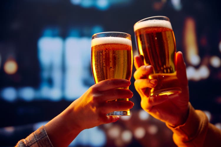 Hands holding lager light frothy large beer glasses and clinking. Two friends are sitting in a bar drinking alcoholic beverages.