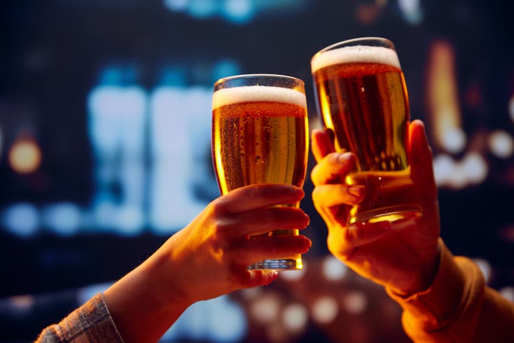 Hands holding lager light foamy big beer glasses and clinking. Two friends sitting in bar and drinking alcohol drinks.