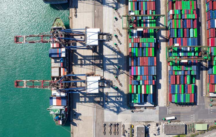 Vertical top down view of cargo containers piled on the quayside and cranes unloading the goods from a ship, which is parking at the dock of Taipei Harbor in Bali District, New Taipei City, Taiwan