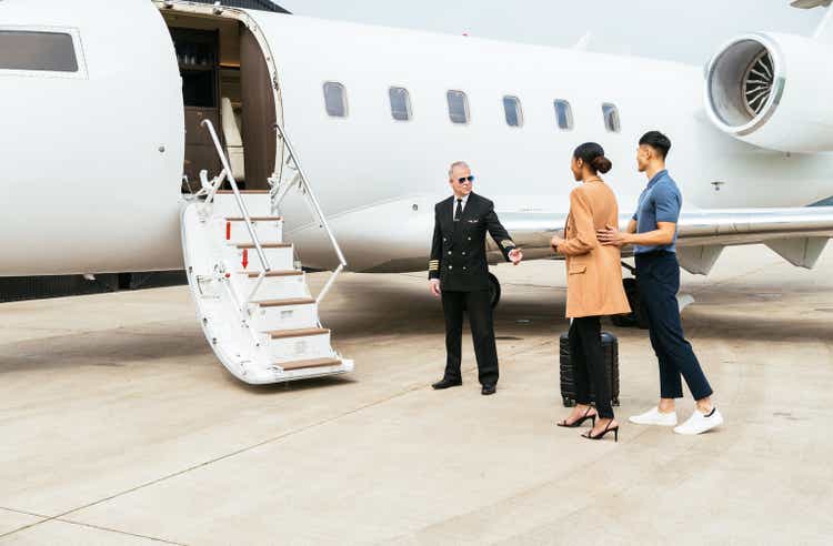 Passengers boarding in private luxury jet near hangar, pilot welcomes the young successful passengers