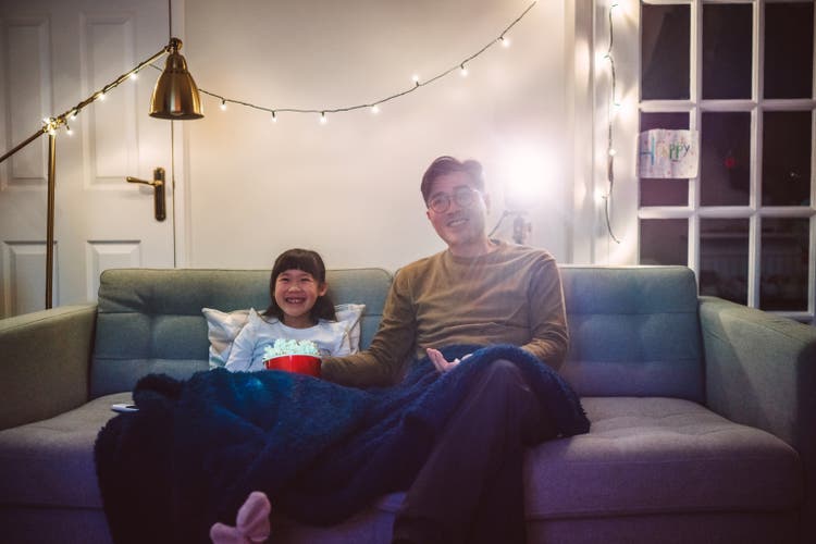 Dad & daughter watching a comedy movie together while eating popcorn during the night at home