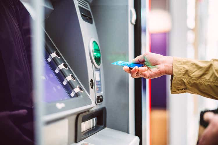 Female hand inserting bank card into automatic cash machine (ATM) to access bank account services in the city