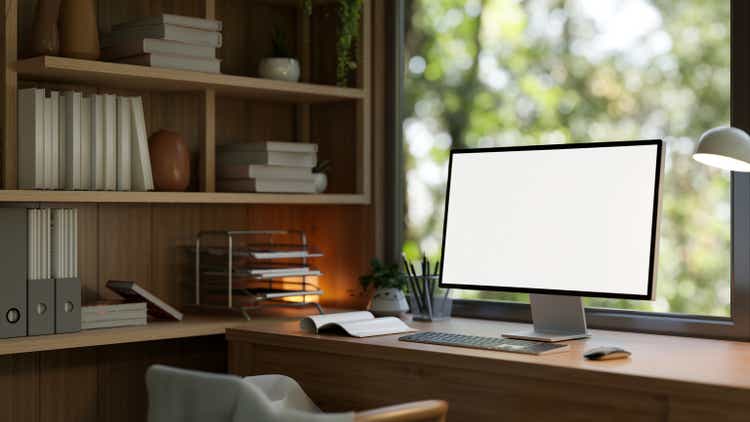 A computer mockup on a wooden desk against the window in a modern and comfortable home office.