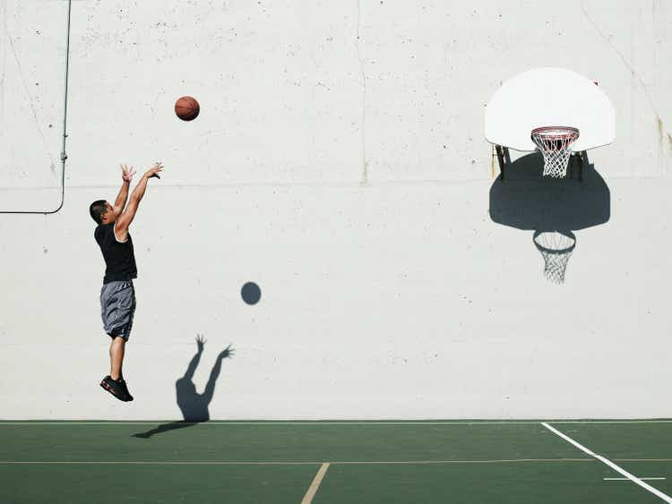 Man shooting jump shot on outdoor basketball court, side view