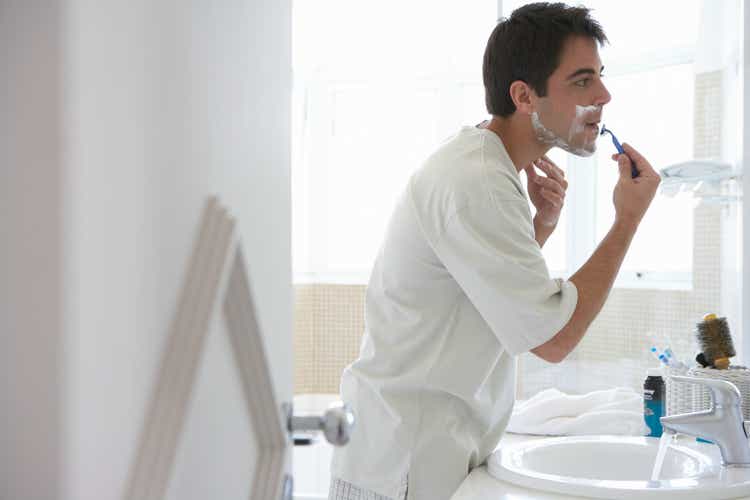 Man shaving face in bathroom mirror, side view