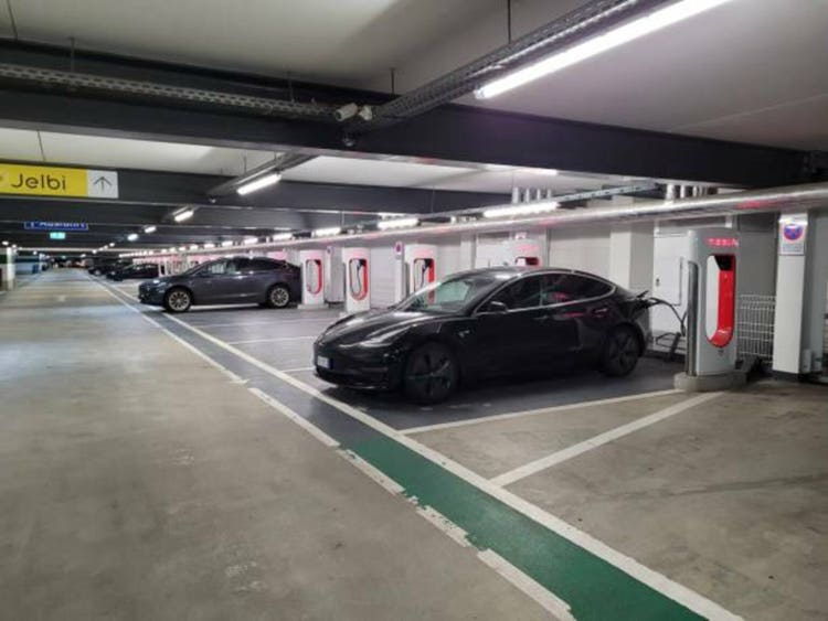 A static shot of a solid black Tesla Model 3 dual motor charging at the Berlin Supercharger in a covered parking lot. Selective focus