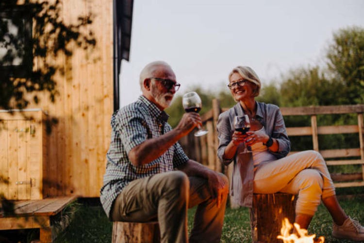 Photo of a senior couple drinking wine by the fire pit in front of the cabin house