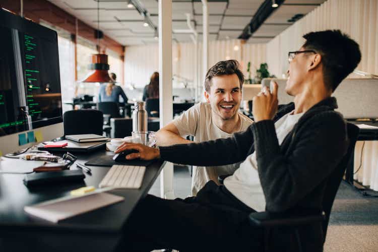Happy multiracial computer programmers laughing while working at tech-startup office