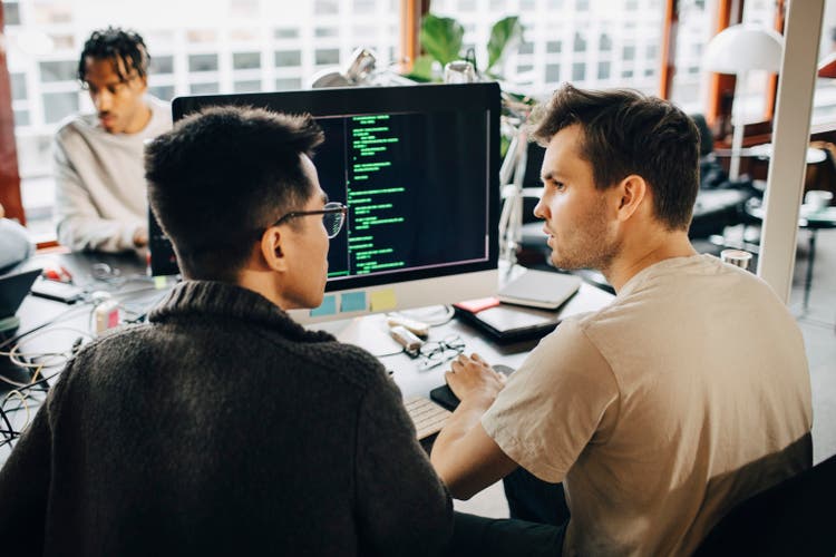 Rear view of male programmers discussing while doing coding on computer at office