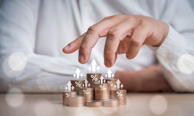 Hand of analyst, investor or trader controls stacking coins at different heights with arrow up and percentage icons for interest rating from each investment, income management. Money planning concept.