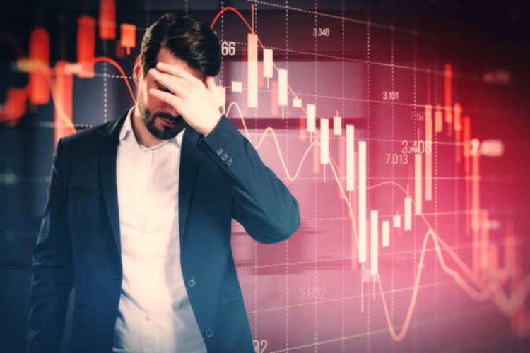 Stressed out man with falling red forex candlestick chart on blurry background. Global economic recession, stock market crash, inflation concept.