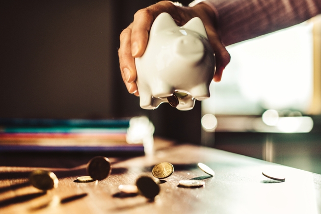 Hand shaking a piggy bank with euro coins falling out.