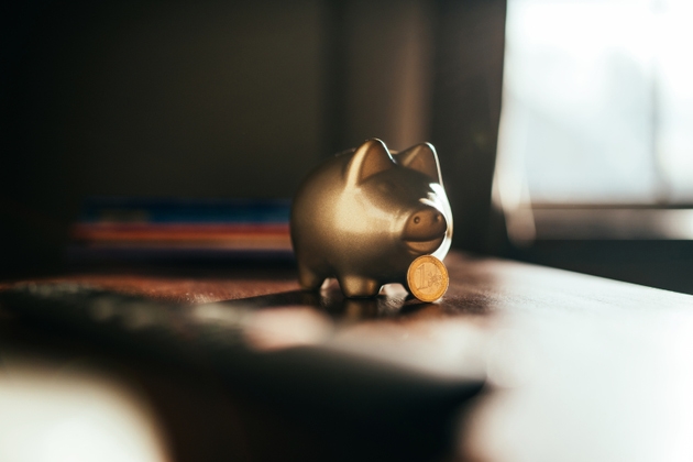 Golden piggybank standing on a table with a euro coin in front.