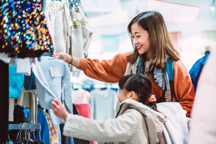 Beautiful Asian mom having fun shopping with her young daughter at clothing store